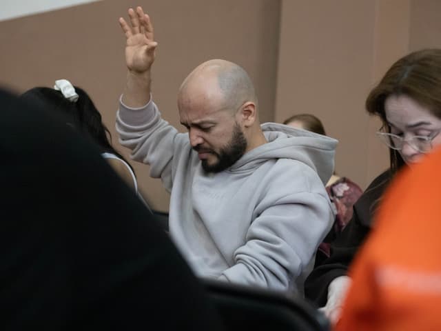 Hombre orando con la mano alzada en medio de la congregación.